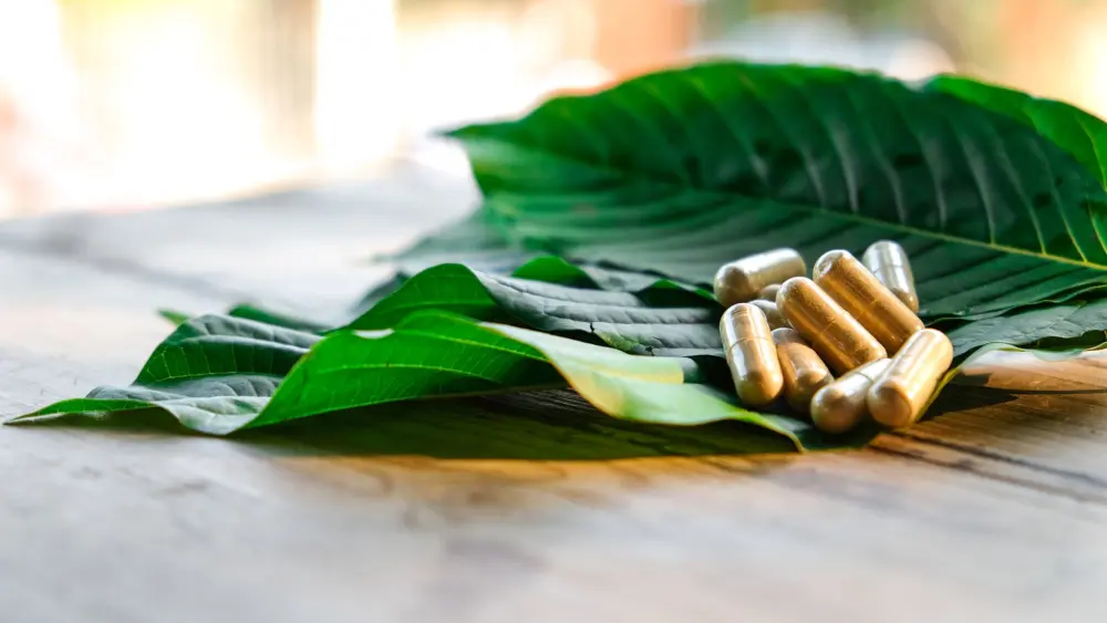kratombladeren op een tafel met kratomcapsules